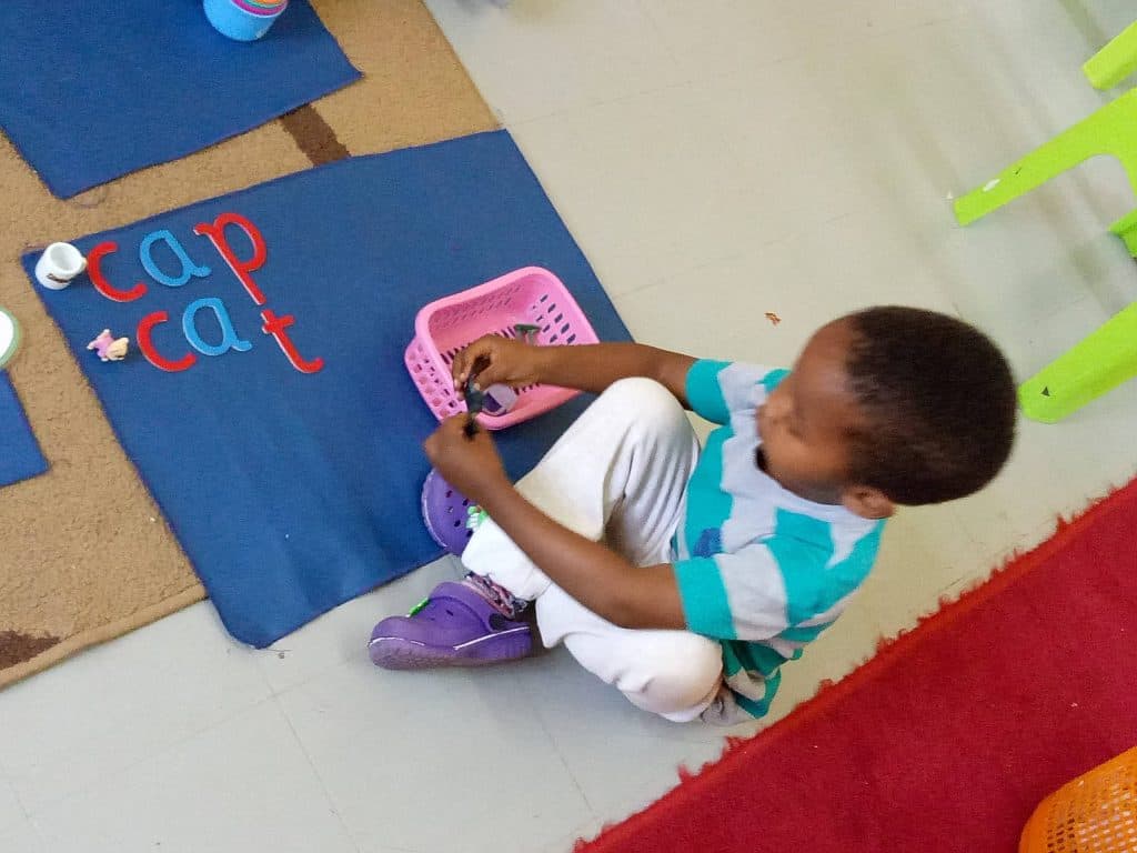 A child building the words 'cap' and 'cat' with a movable alphabet on a work mat